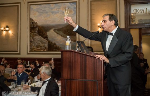 a speaker at a corporate event raising his glass for a toast at the podium