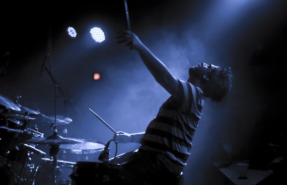 a photo of a drummer perofrming live, raising his arm in the air