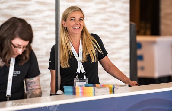 a woman smiling at the registration desk of a conference