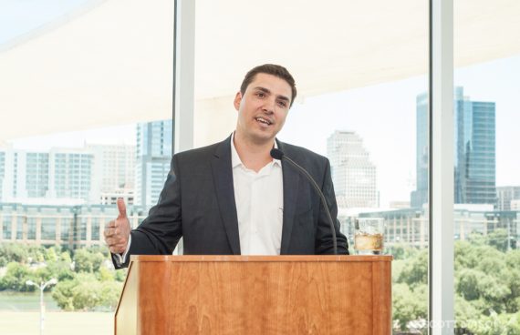 a corporate event photo of a sharp-dressed man giving a speech at a podium