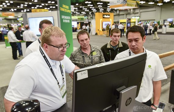 a photo of men looking at a computer screen in the exhibit hall of the Austin Convention Center the