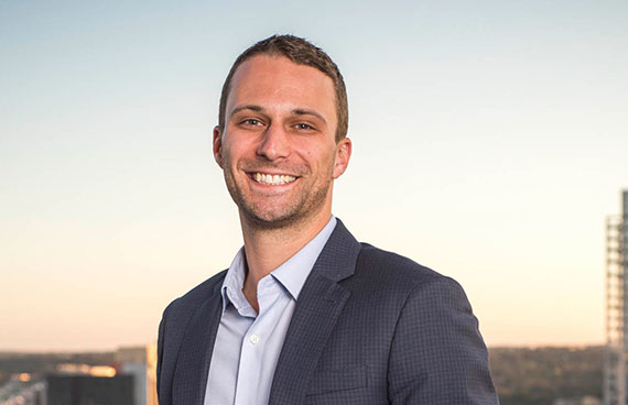 a business portrait/headshot of a smiling man standing on a rooftop downtown