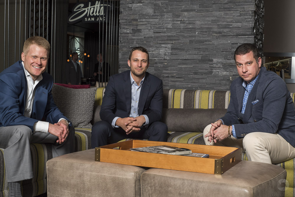 a photo of three men in business suits sitting at a table having a meeting, looking into the camera