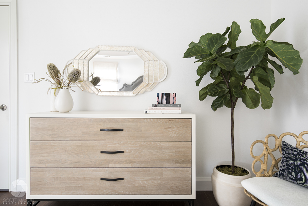 a one-point perspective interior design photo of a dresser, plant and chair against a white wall with a mirror on it