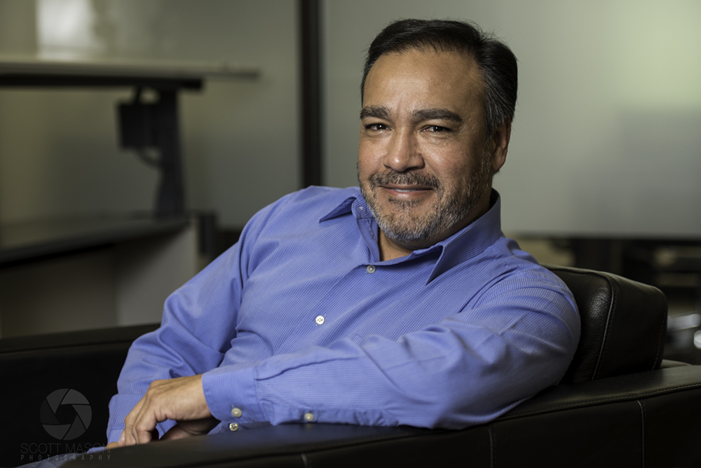 a corporate portraits of a man leaning on a chair, smiling