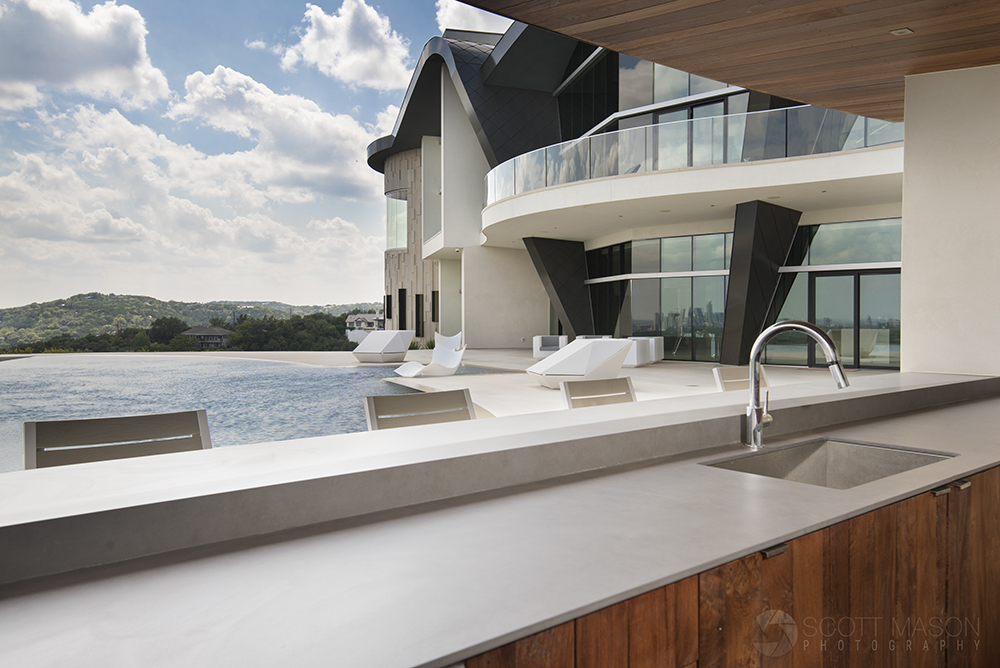 an exterior architectural photo with an outdoor bar in the foreground and a large house in the background