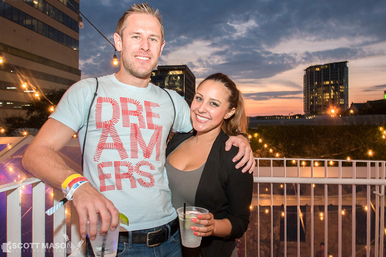 a photo of a couple standing on a deck with the sunset behind them, smiling at the camera