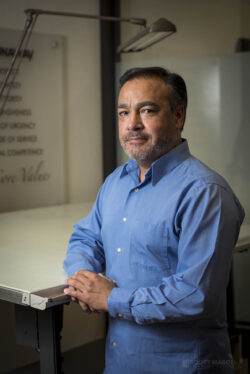 a business portrait/headshot of a man standing next to his drafting table in an office