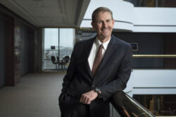 a business portrait of a smiling middle-aged man leaning on a railing in an office building
