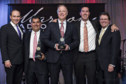 a group photo of five men holding their awards on stage, posed