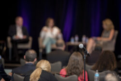 a close-up of a microphone with panelists in the background